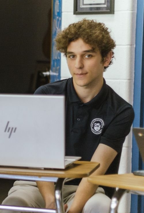 male student sitting in classroom desk with laptop